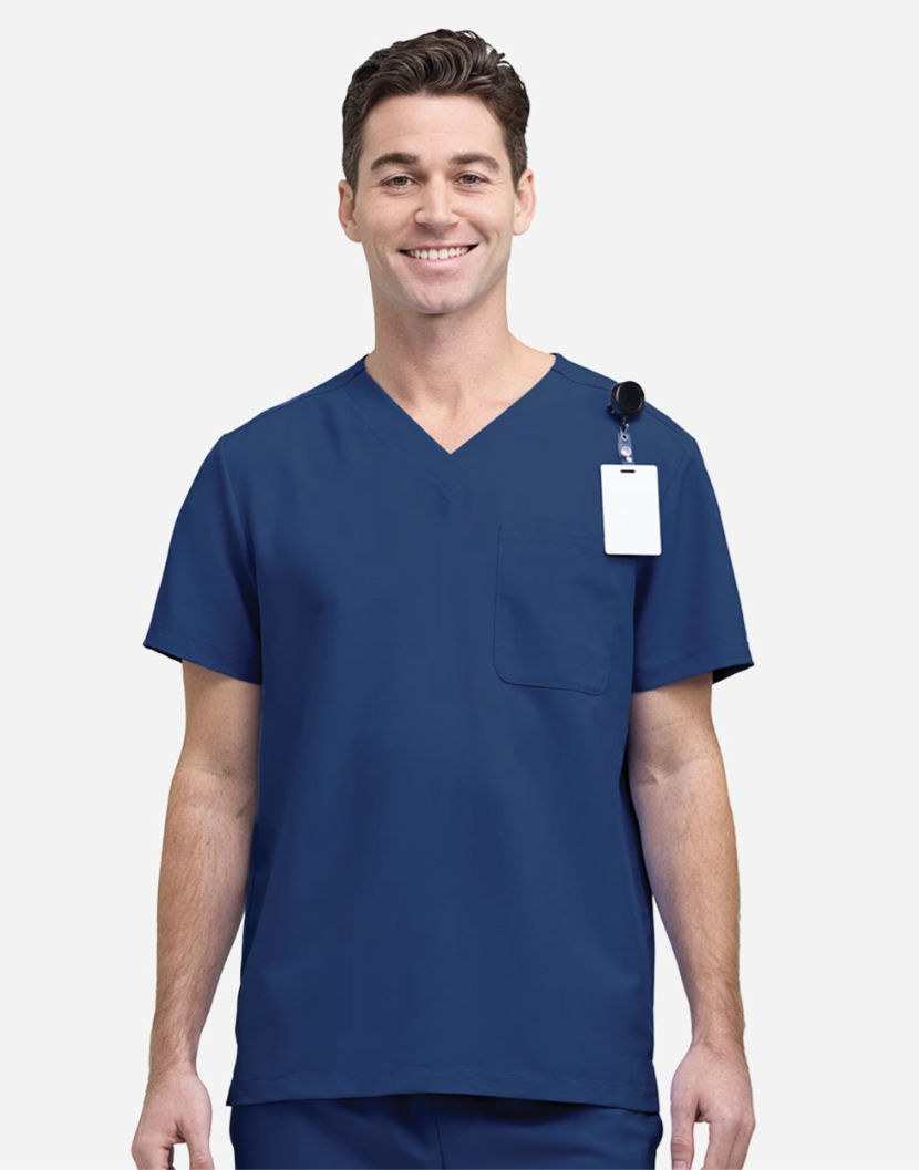 A smiling man wearing a navy blue V-neck scrub top with a chest pocket and a white ID badge clipped to the shoulder, photographed against a light gray studio background.